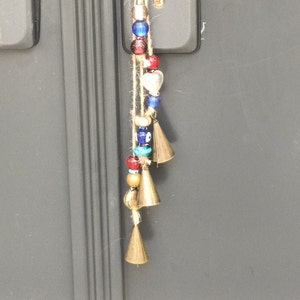 Puede incluir: Una cadena de cuentas con detalles azules, rojos y blancos cuelga de una puerta. Las cuentas están unidas a pequeñas campanas doradas.