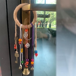 Może przedstawiać: Łapacz snów wykonany z makramu z drewnianym pierścieniem, koralikami i zawieszkami. Łapacz snów jest przymocowany do klamki.