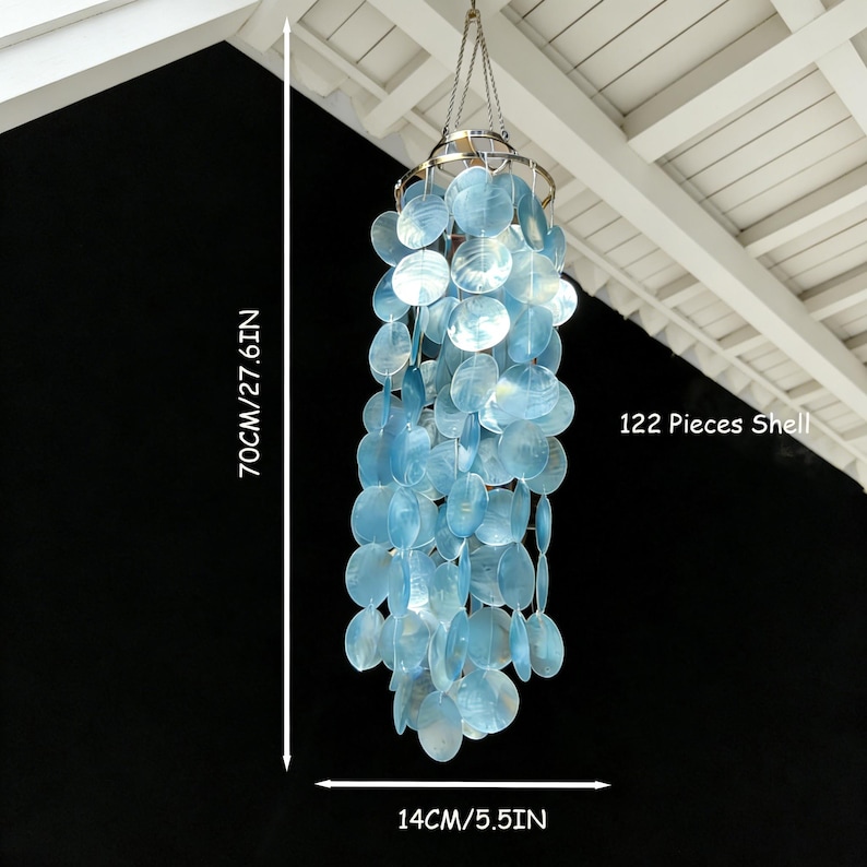 May include: A hanging wind chime made of 122 blue shell pieces. The chime is 27.6 inches long and 5.5 inches wide. It hangs from a metal ring and chain. The text "122 Pieces Shell" is visible.