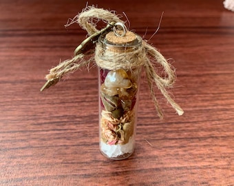 May include: A small glass bottle with a cork top and a key charm attached. The bottle is filled with dried flowers, crystals, and other natural elements.