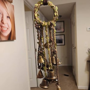 May include: A green and brown wreath with a ring of woven rope and a series of small brass bells hanging from it.