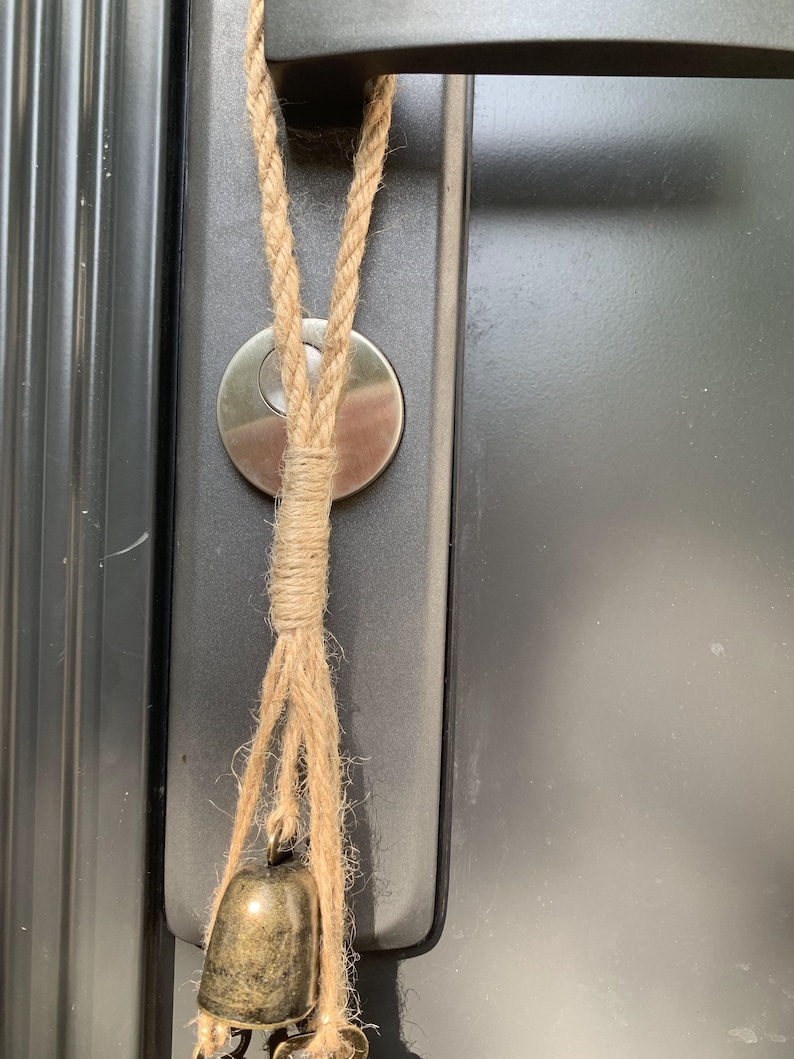 May include: A brown rope with a small gold bell hanging from it. The rope is tied to a door handle.