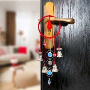 Puede incluir: Un atrapasueños rojo y plateado con campanas y cristales colgando de una cuerda roja. El atrapasueños está sujeto a un pomo de puerta.
