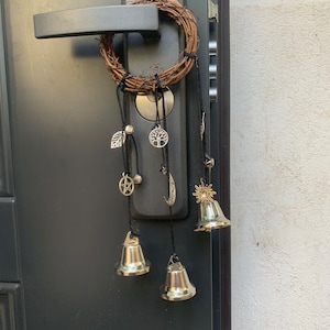 May include: A door with a wreath hanging on the handle. The wreath has several charms hanging from it, including bells, a crescent moon, a star, a tree, and a pentagram. The charms are silver and gold.