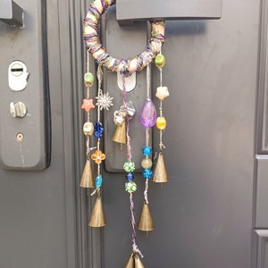 Könnte beinhalten: Ein bunter Traumfänger mit Perlen und Glöckchen, die an einem gewebten Ring hängen. Der Traumfänger ist an einem Türgriff befestigt.