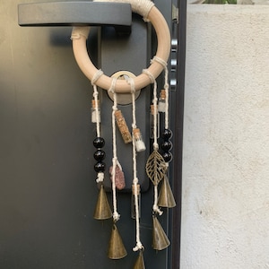 Op de afbeelding: Een houten ring omwikkeld met touw, versierd met hangende glazen flesjes, zwarte kralen, een metalen blad en messing bellen. De flesjes bevatten diverse gedroogde kruiden en kristallen, waardoor een decoratief stuk in bohemien stijl ontstaat.