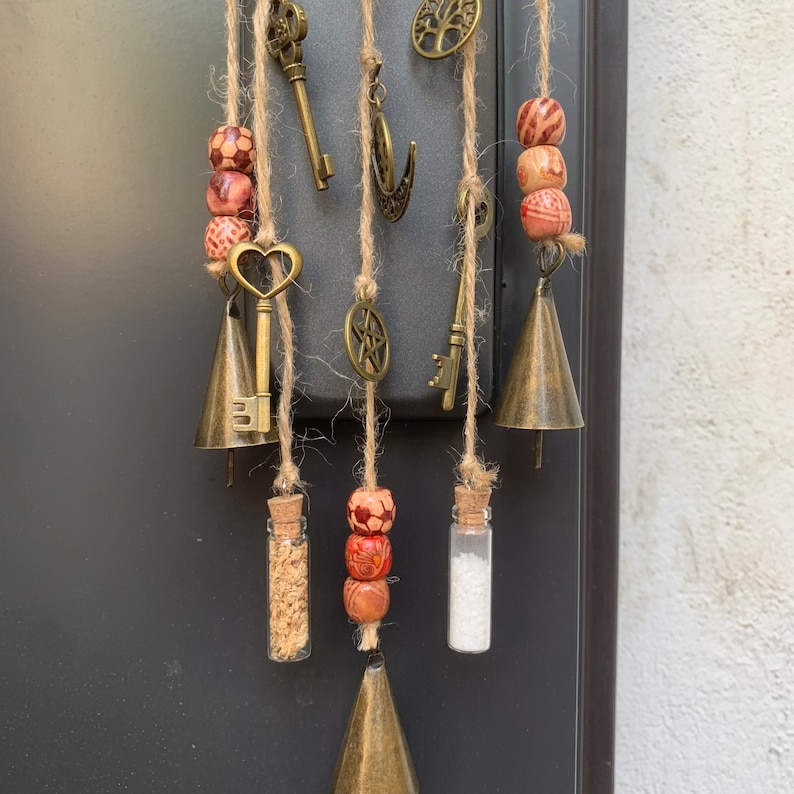 May include: A wind chime with multiple strands of twine, each with a variety of charms, including keys, bells, and small glass vials. The charms are interspersed with wooden beads with a red and brown pattern.