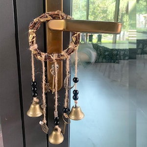 May include: A gold door handle with a wreath-shaped dream catcher hanging from it. The dream catcher has black beads, bells, and a crescent moon charm.