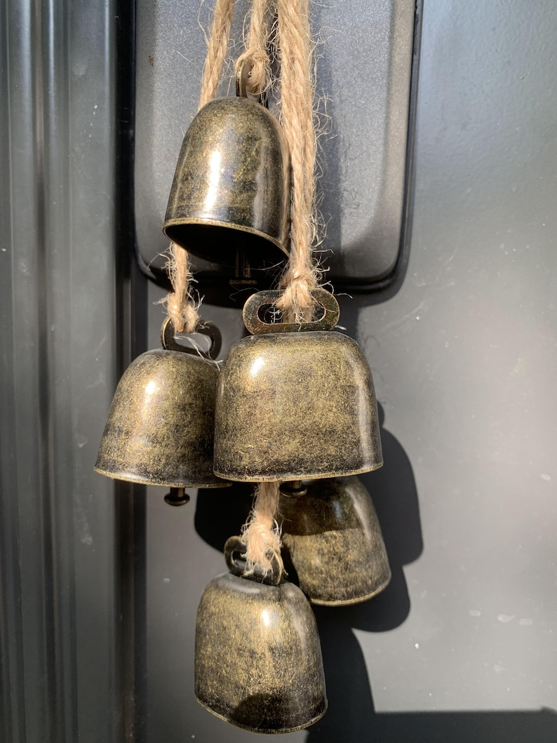May include: A set of five antique gold-toned bells hanging from a twine string. The bells are different sizes and have a distressed finish.
