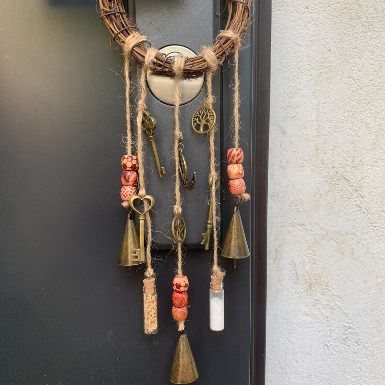 May include: A brown and beige dream catcher with wooden beads, bells, and keys hanging from it. The dream catcher is attached to a door with a brown wooden frame.