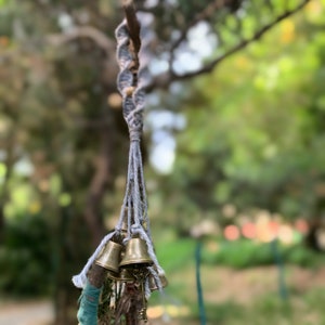 以下が含まれることがあります： 木の枝からぶら下がっている、小さな金のベルの集まりが付いた灰色のマクラメの紐