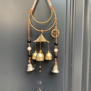 May include: A gold wind chime with a wooden and black bead strand, a gold ring, and a small gold roof. The chime has five silver bells and a small silver bell hanging from the bottom.