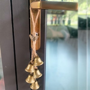 K&ouml;nnte beinhalten: Ein goldener T&uuml;rgriff mit einer Schnur aus kleinen goldenen Glocken, die daran h&auml;ngen. Die Glocken sind an einer braunen Bindfaden-Schnur mit einem kleinen Schmetterlingsanh&auml;nger oben befestigt.