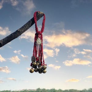 May include: A red tassel with a gold star charm and multiple small bells hanging from a branch against a blue sky with white clouds.