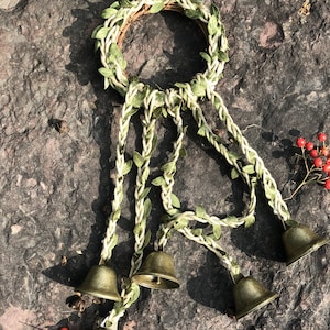 May include: A wreath made of green leaves and twine with four small brass bells hanging from it.