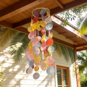 May include: A colorful wind chime with multiple circular, iridescent pieces in shades of pink, yellow, blue, and red. The chime is suspended from a wooden ring and hangs in front of a wooden ceiling and a white wall.