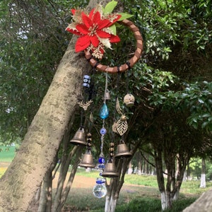 Puede incluir: Un atrapasueños de madera con una flor de poinsettia roja, cuentas azules y negras, campanas y un prisma de cristal colgando.