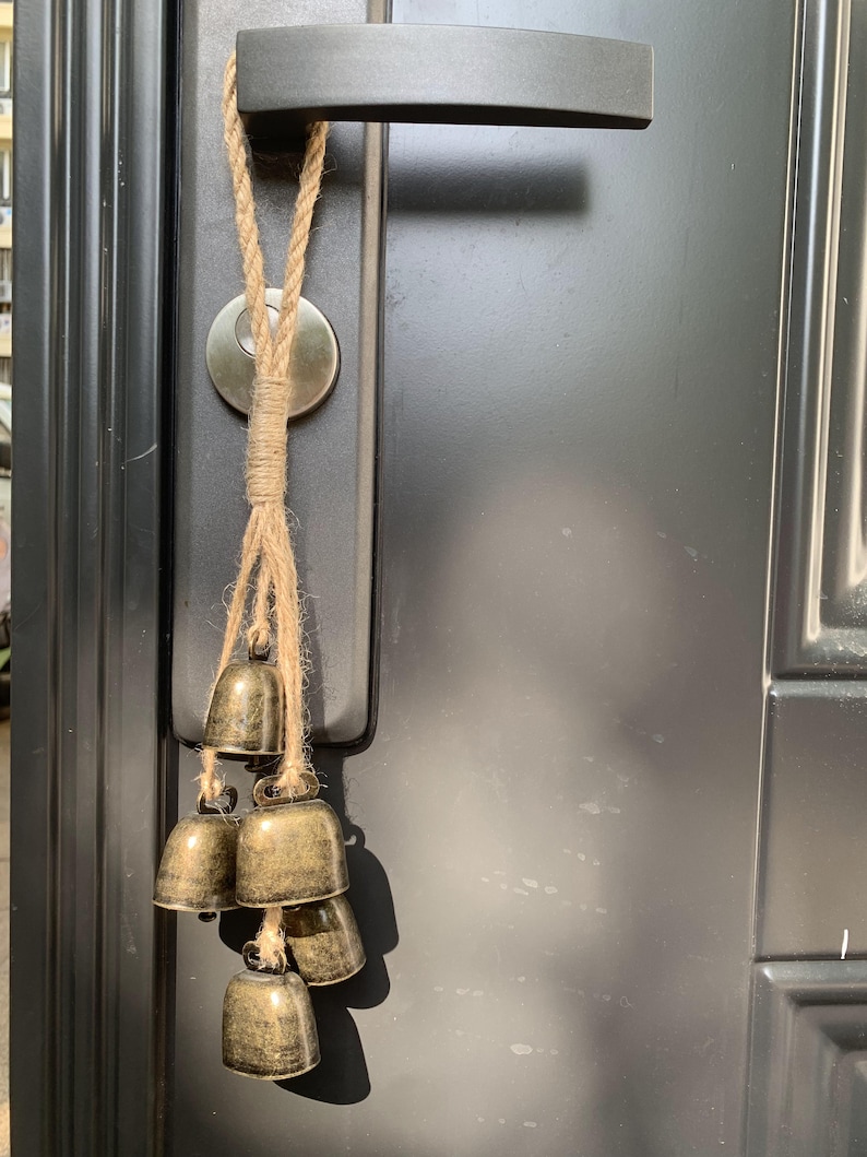 May include: A set of small, gold-colored bells hanging from a door handle. The bells are attached to a length of natural twine.