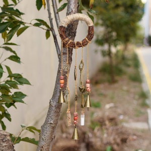 May include: A rustic-style wind chime with a woven twig ring, hanging from a tree branch. The chime features multiple strands with small bells, keys, beads, and a charm with a tree of life design.