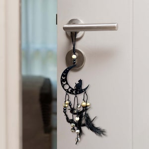 Könnte beinhalten: Schwarzer und goldener Traumfänger mit einem Halbmond und einer schwarzen Katzensilhouette, der an einem Türknauf hängt. Der Traumfänger hat Federn und Glöckchen.