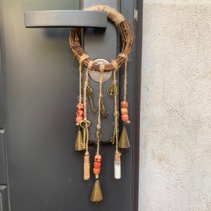 May include: A brown twig wreath with a variety of charms hanging from it, including keys, bells, and beads. The wreath is hanging on a door.