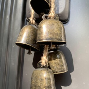 May include: A set of five antique gold-toned bells hanging from a twine string. The bells are various sizes and have a distressed finish.
