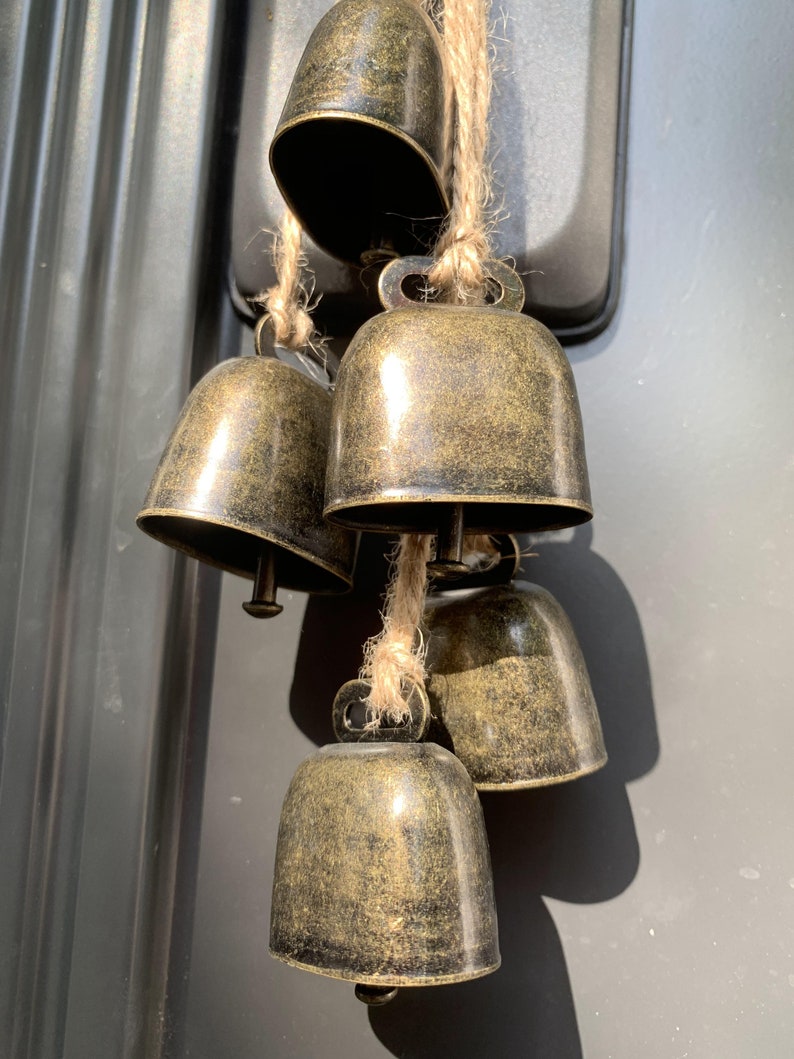 May include: A set of five antique gold-toned bells hanging from a twine string. The bells are various sizes and have a distressed finish.