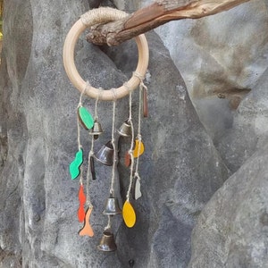Könnte beinhalten: Ein Holzring mit verschiedenen bunten Formen und kleinen Glocken, die daran hängen. Der Ring ist an einem Ast befestigt und die Glocken hängen herunter.