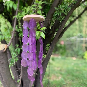 May include: Purple wind chime made of round, translucent, overlapping discs hanging from a wooden ring.
