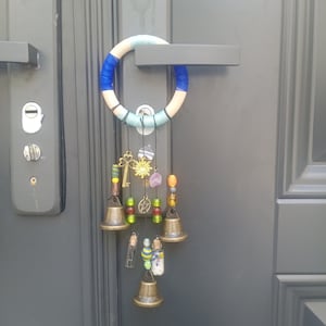 Könnte beinhalten: Ein blauer, weißer und grüner Makramee-Traumfänger mit Glöckchen, Perlen und Charms, die daran hängen. Der Traumfänger ist an einem Türgriff befestigt.