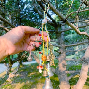Könnte beinhalten: Eine bunte Glockenkette mit verschiedenen Anhängern, darunter ein Schlüssel, ein Pilz und ein Kolibri. Die Glocken hängen an einem Ast.