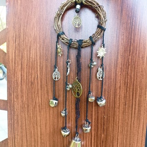 May include: A dream catcher with a woven twig hoop, black lace, and multiple silver bells hanging from it. The hoop has a small tree of life charm and two sun charms.
