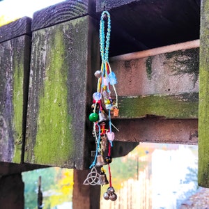 以下が含まれることがあります： 木製の表面からぶら下がっている、ベル、ビーズ、その他の装飾的な要素が付いたカラフルなチャームの紐。チャームは青、緑、赤、ピンクが混ざっています。