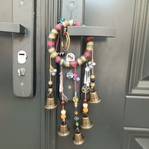 以下が含まれることがあります： ビーズのフリンジと小さなベルがぶら下がったカラフルなドリームキャッチャー。ドリームキャッチャーはドアノブに取り付けられています。