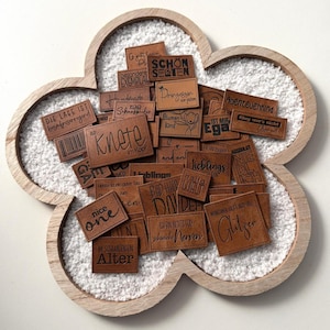 Könnte beinhalten: Eine Sammlung brauner Lederpatches mit verschiedenen deutschen Sprüchen darauf gedruckt, wie "Schon Selten", "Prinzessin", "Knote", "Abenteuerkind", "Lieblings", "Bad Hair Day", "Im Schwierigen Alter" und "Glitzern".