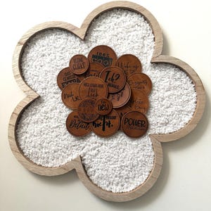 Könnte beinhalten: Ein hölzerner, blumenförmiger Tablett mit einer weißen, flauschigen Oberfläche. Das Tablett ist gefüllt mit kleinen braunen Lederflicken mit verschiedenen deutschen Sätzen darauf gedruckt, wie "100% Kohle", "Kleine Gurke", "Das Gewisse", "Lie", "Ich?", "Niemals", "Mich Kann Man", "Im Lie", "New", "Besser", "Einzigartig", "Lets", "Gang", "Detail", "Nicht", und "Power".