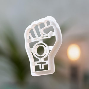 Può includere: Tagliapasta in plastica bianca a forma di pugno con il simbolo femminile all'interno.