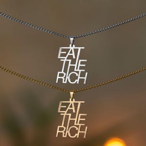Puede incluir: Dos collares con un colgante plateado y dorado que dice "Eat the Rich".