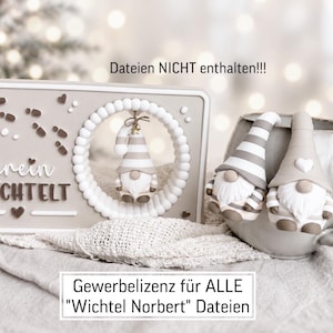 Könnte beinhalten: Ein rechteckiges beiges Schild mit dem Text "Herein GEWICHTELT" und braunen Fußabdruck-Symbolen, das einen kreisförmigen Ausschnitt mit einem hängenden Wichtelornament aufweist. Daneben steht eine Keramiktasse mit zwei kleinen Wichtelfiguren.