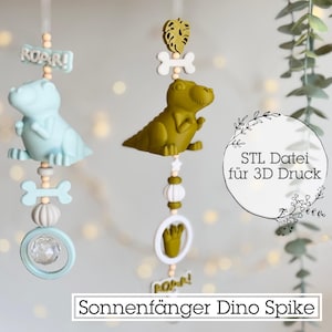 May include: Three hanging dinosaur-themed suncatchers. One is light blue, the other is olive green. Each has a dinosaur figure, bone-shaped accents, and the word "ROAR!" on a sign. The text "STL Datei für 3D Druck" is also visible.