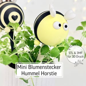 Op de afbeelding: Een grillige plantenstaak met een geel en zwart bijenontwerp en witte accenten. De bijvormige staak staat in een pot met groene planten. De tekst "Mini Blumenstecker Hummel Horstie" is zichtbaar.