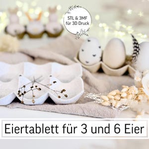 Op de afbeelding: Een witte eiertray voor 3 en 6 eieren, met decoratieve eieren en bloemaccenten. De afbeelding bevat de tekst "STL & 3MF für 3D Druck". De eieren zitten in een kartonnen eierdoos. Het algemene thema is Pasen.