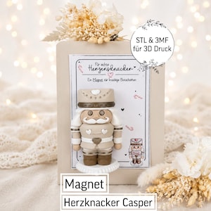 Puede incluir: Un imán de cascanueces beige con detalles en blanco y marrón, exhibido en una tarjeta rectangular con el texto "Für echte Herzensknacker" y "Ein Magnet für knackige Botschaften". Una etiqueta circular dice "STL & 3MF für 3D Druck".