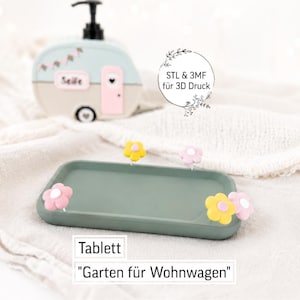 Peut inclure: Un plateau rectangulaire vert sauge orné de petites fleurs jaunes et roses. En arrière-plan, un distributeur de savon bleu clair et beige en forme de caravane avec une pompe noire porte l'inscription Seife sur le côté.