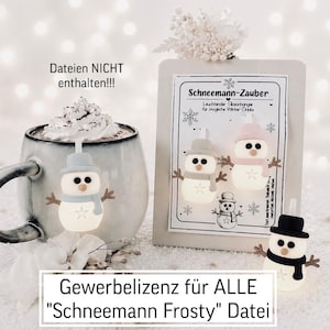 May include: Three small snowman-shaped light-up ornaments with hats and scarves in grey, pink, and black. One snowman hangs on a ceramic mug filled with a drink, while two others are displayed on a card labelled Schneemann-Zauber.