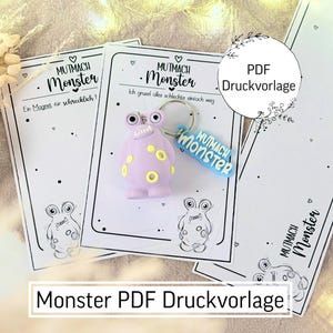 Könnte beinhalten: Mehrere weiße Karten mit schwarzen Illustrationen und Text, zusammen mit einem lila Monster-Schlüsselanhänger mit gelben Details. Auf den Karten stehen die Wörter "MUTMACH Monster" und "Monster PDF Druckvorlage".
