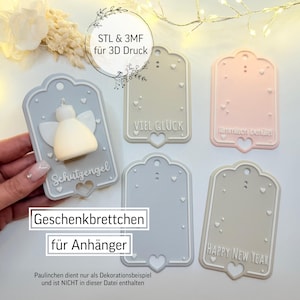 May include: A collection of decorative gift tags in various pastel colors, including gray and pink. Some tags feature text like "Happy New Year" and "Viel Glück". One tag has a small angel figurine. The tags are designed for 3D printing.