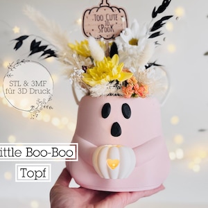 Op de afbeelding: Een roze spookvormige pot met zwarte ogen en mond, met een pompoen. De pot is gevuld met gele, witte en oranje bloemen. De tekst "Too Cute to Spook" staat op een pompoenvormig bord.