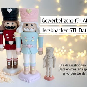Puede incluir: Tres figuras decorativas de cascanueces en rojo, azul y beige, con detalles de corazón. Las figuras están sobre bases en forma de corazón. El texto de la imagen dice "Gewerbelizenz für ALLE Herzknacker STL Dateien" y "Die dazugehörigen STL Dateien müssen separat erworben werden!!"