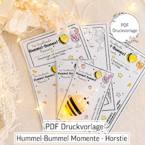 May include: A set of printed cards featuring illustrations of a bumblebee and a cocktail glass with the text "F&uuml;r leuchtende Hummel-Bummel Momente". A small, yellow and black striped bumblebee figurine with a glowing light is placed on top.